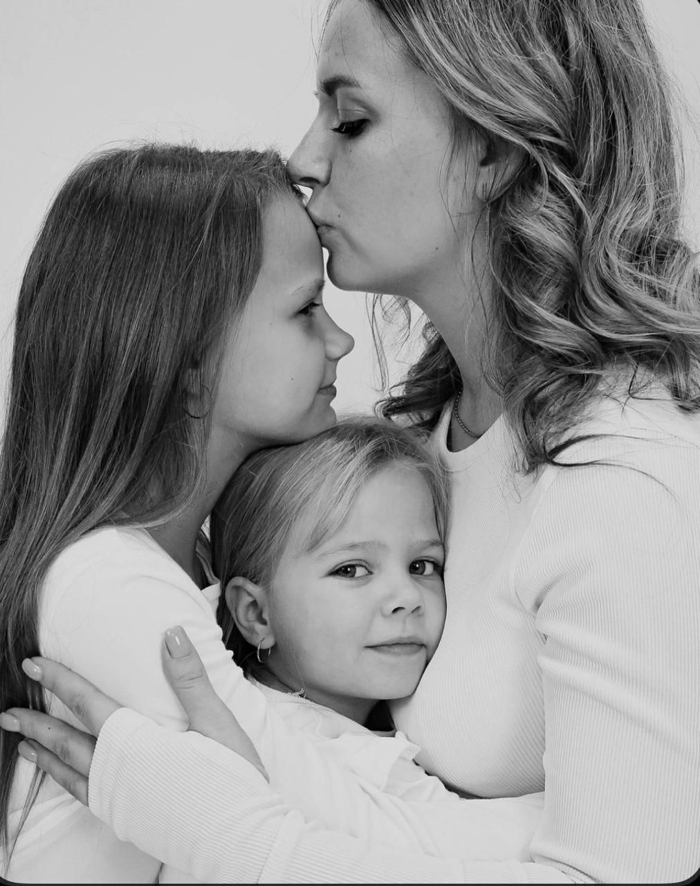 A tender black and white portrait showing a loving moment between a parent and two children.