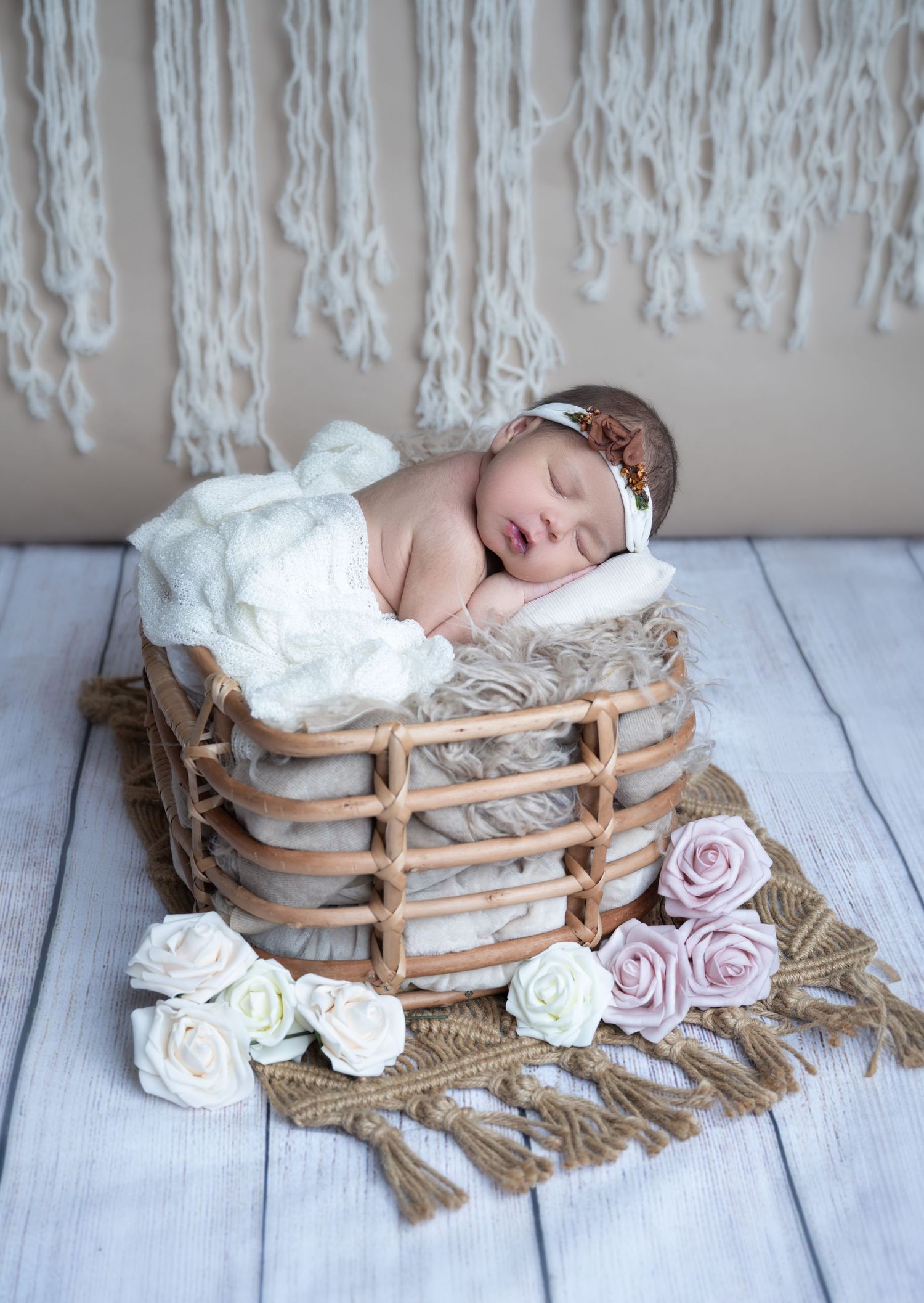 Artistic newborn photo in rustic basket with delicate roses and macrame backdrop.