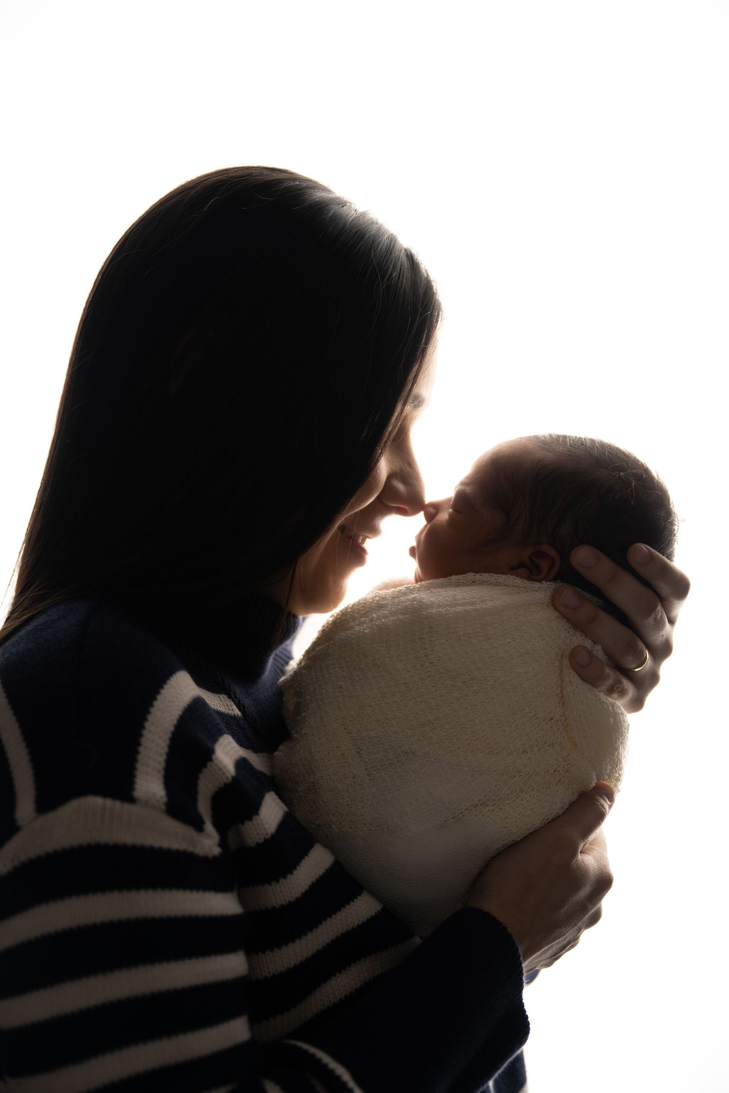Silhouette of parent and newborn sharing an intimate bonding moment against white background.
