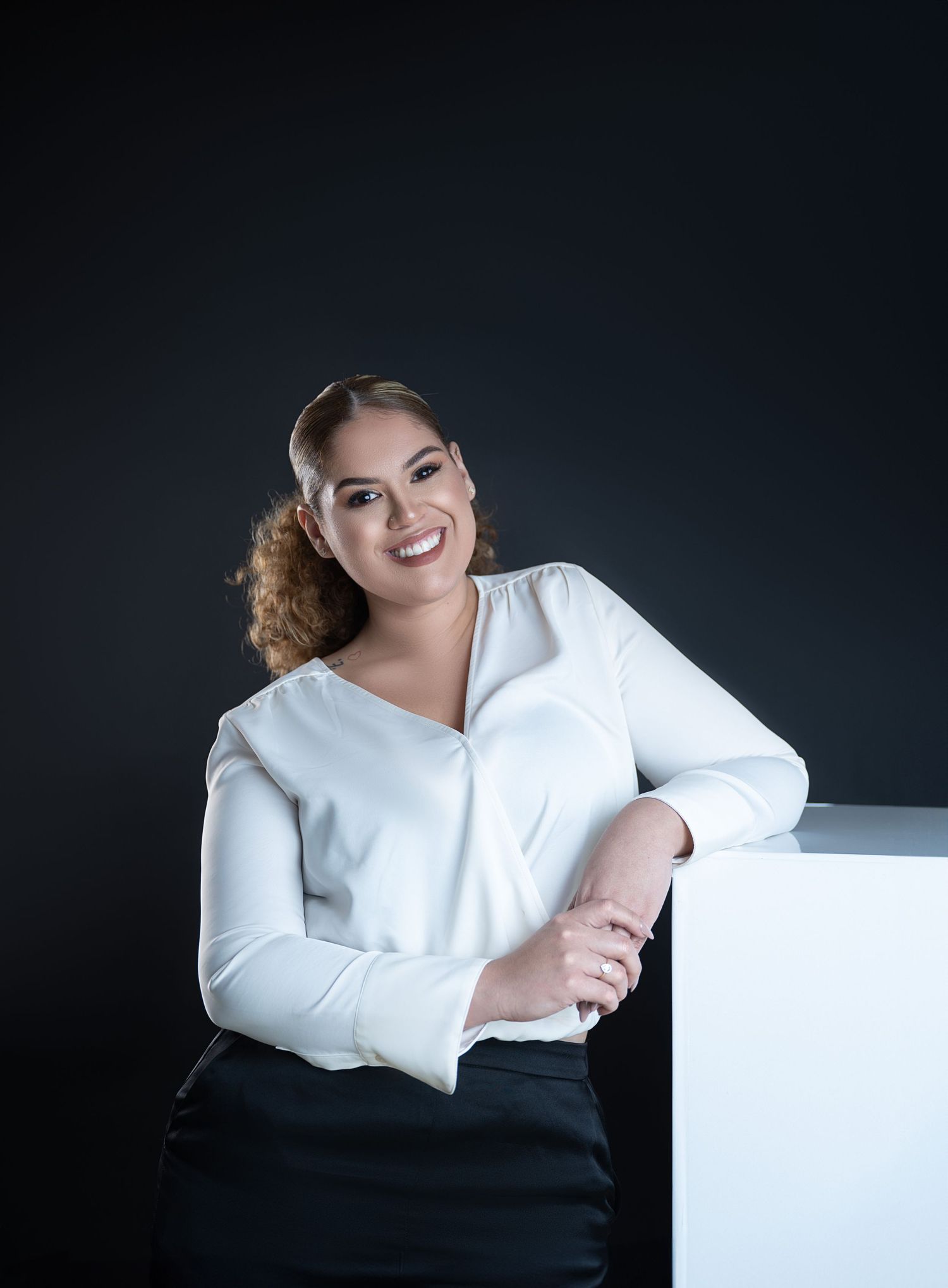 Professional studio portrait in white blouse against dark background.