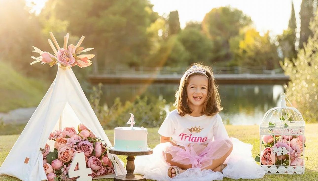 Girl in pink tutu celebrates 4th birthday outdoors with floral decor, teepee, and birdcage in garden setting.
