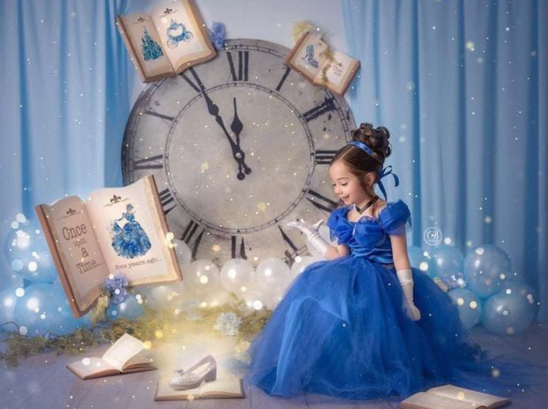 A young girl in a blue ball gown reads a book beside a large clock in a magical Cinderella-themed fantasy setting.