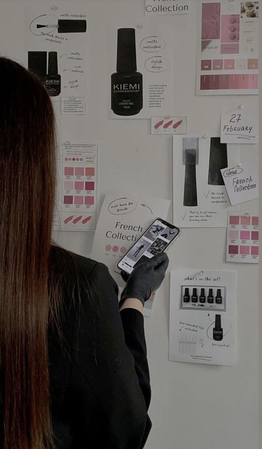 Woman in black gloves holds phone near a mood board featuring KIEMI French Collection nail gel products and color swatches.