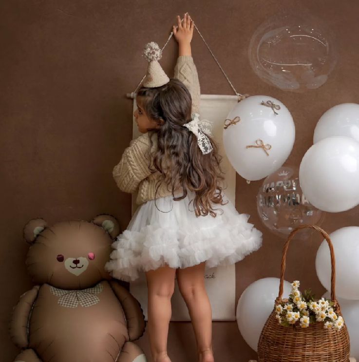 A dreamy party scene with balloons, teddy bear and basket against a brown backdrop.