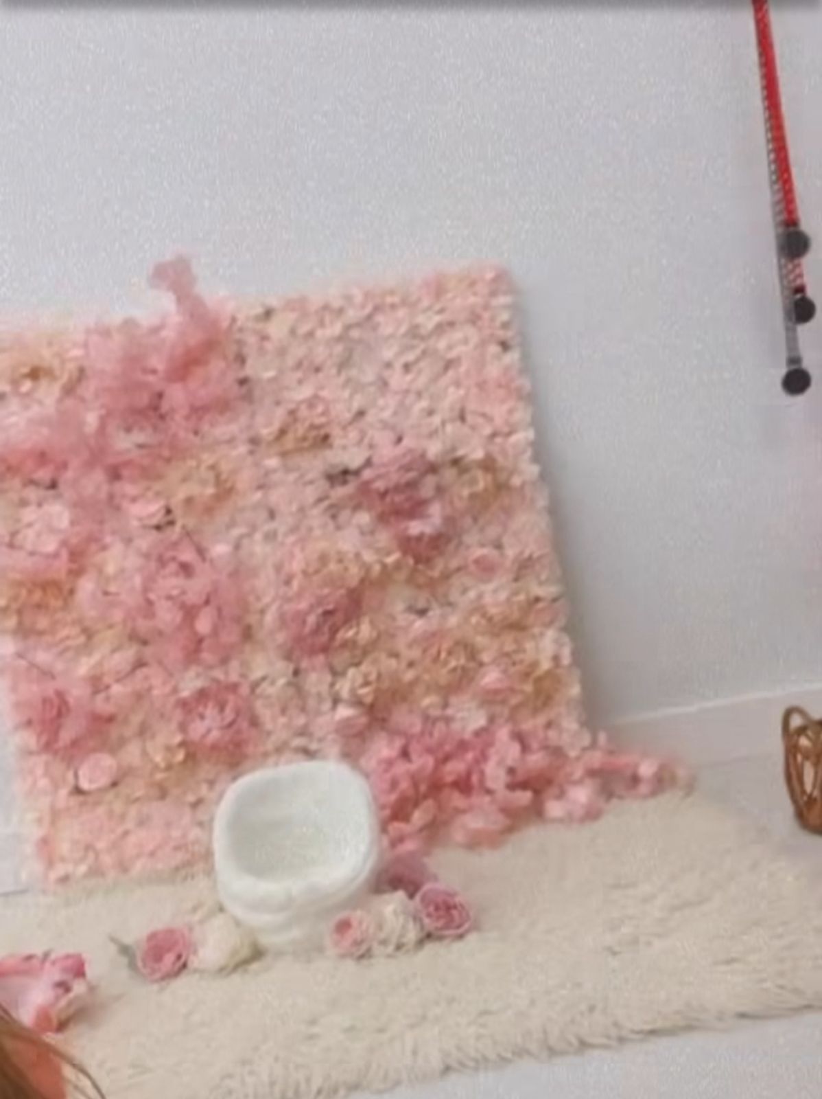 Pink floral backdrop setup with white cushion and scattered rose petals for photography.