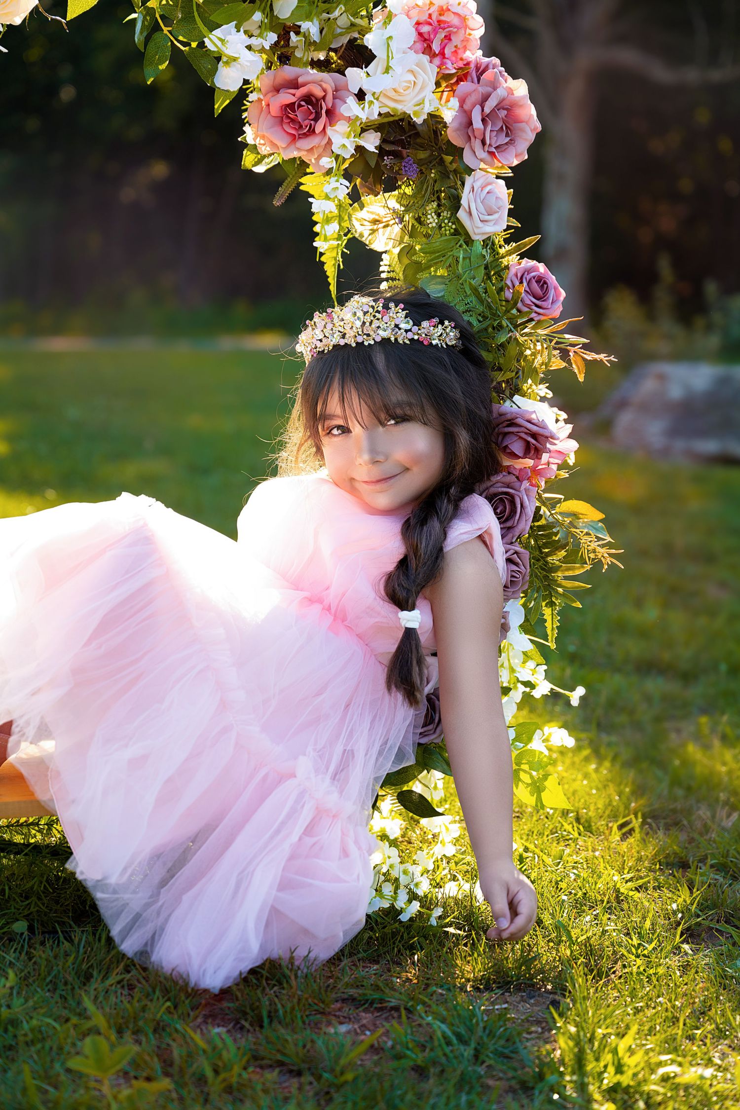 A dreamy garden portrait with pink tulle dress and floral arch in golden sunlight.