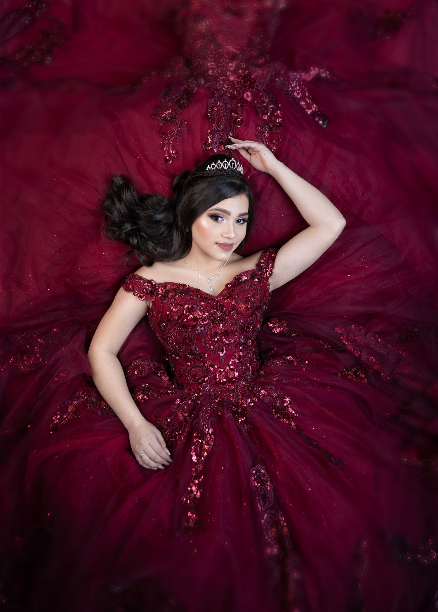 Glamorous portrait in burgundy ball gown with sequins against deep red background.
