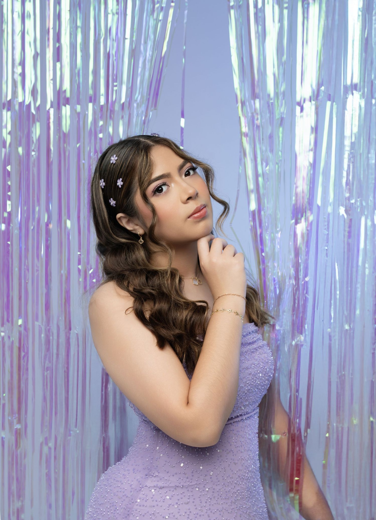 Young woman in lavender sequin dress poses against iridescent tinsel backdrop with star hair accessories.