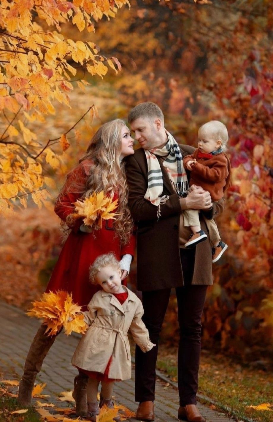 Family enjoying autumn scenery with golden leaves and red foliage in a beautiful outdoor setting.
