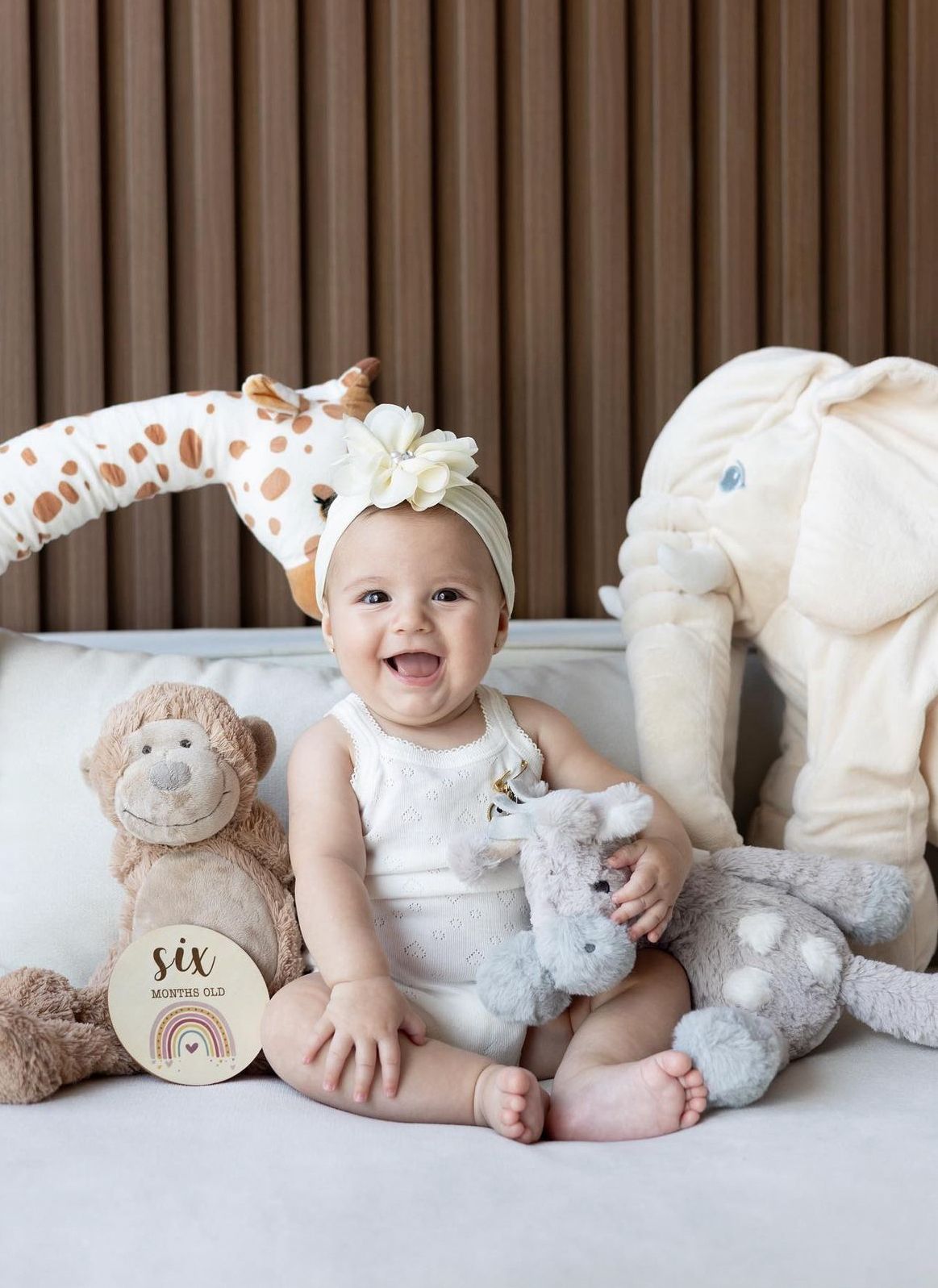 Nursery scene with plush stuffed animals including giraffe, monkey, and elephant on white couch.