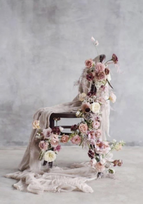 Vintage sewing machine decorated with delicate pink roses and flowing fabric against grey backdrop.