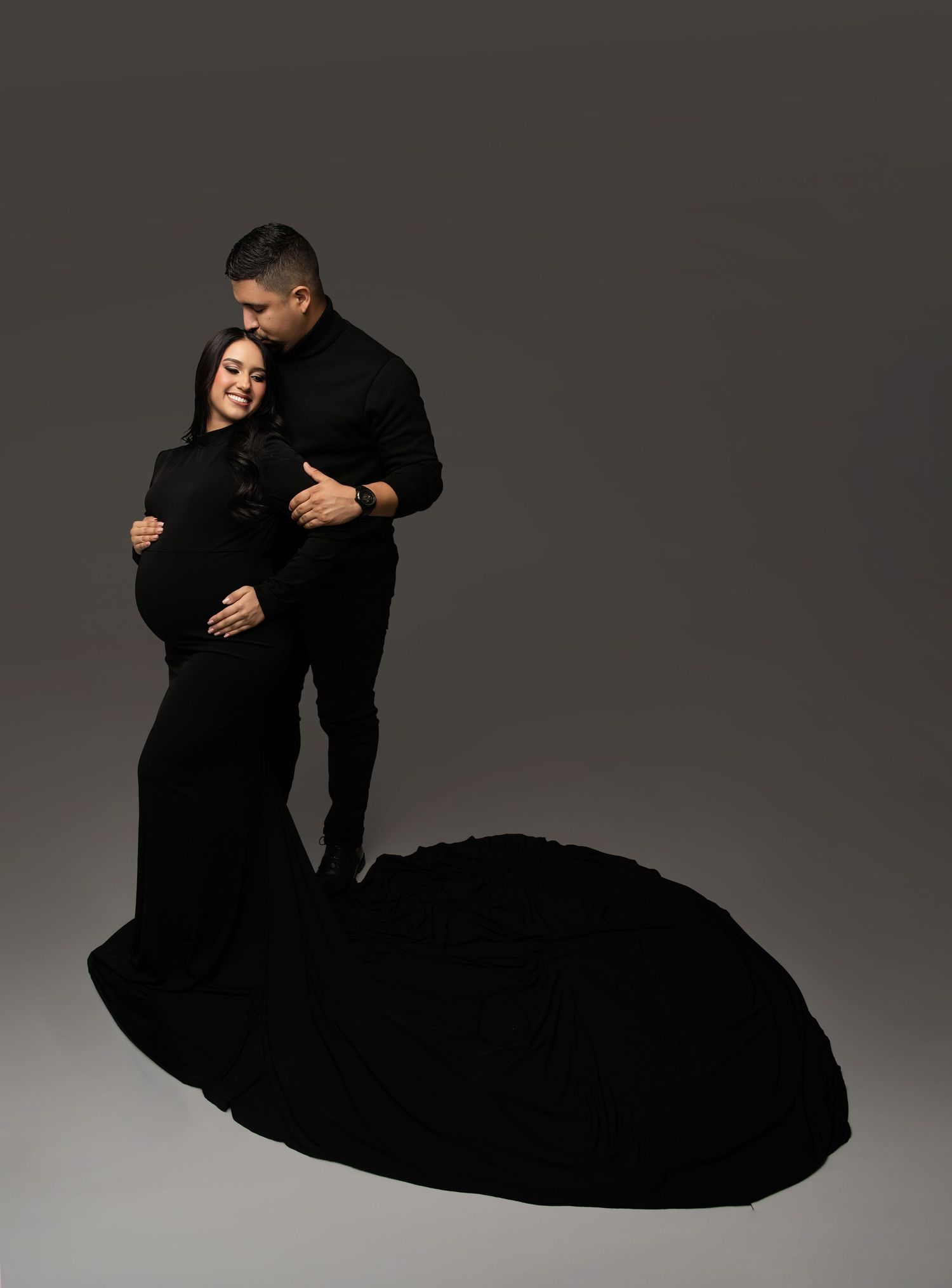 Two figures in black attire perform a dramatic dance lift against a gray studio backdrop.