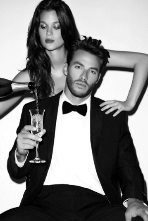 A black and white glamour photo showing a couple in formal attire with a champagne glass.