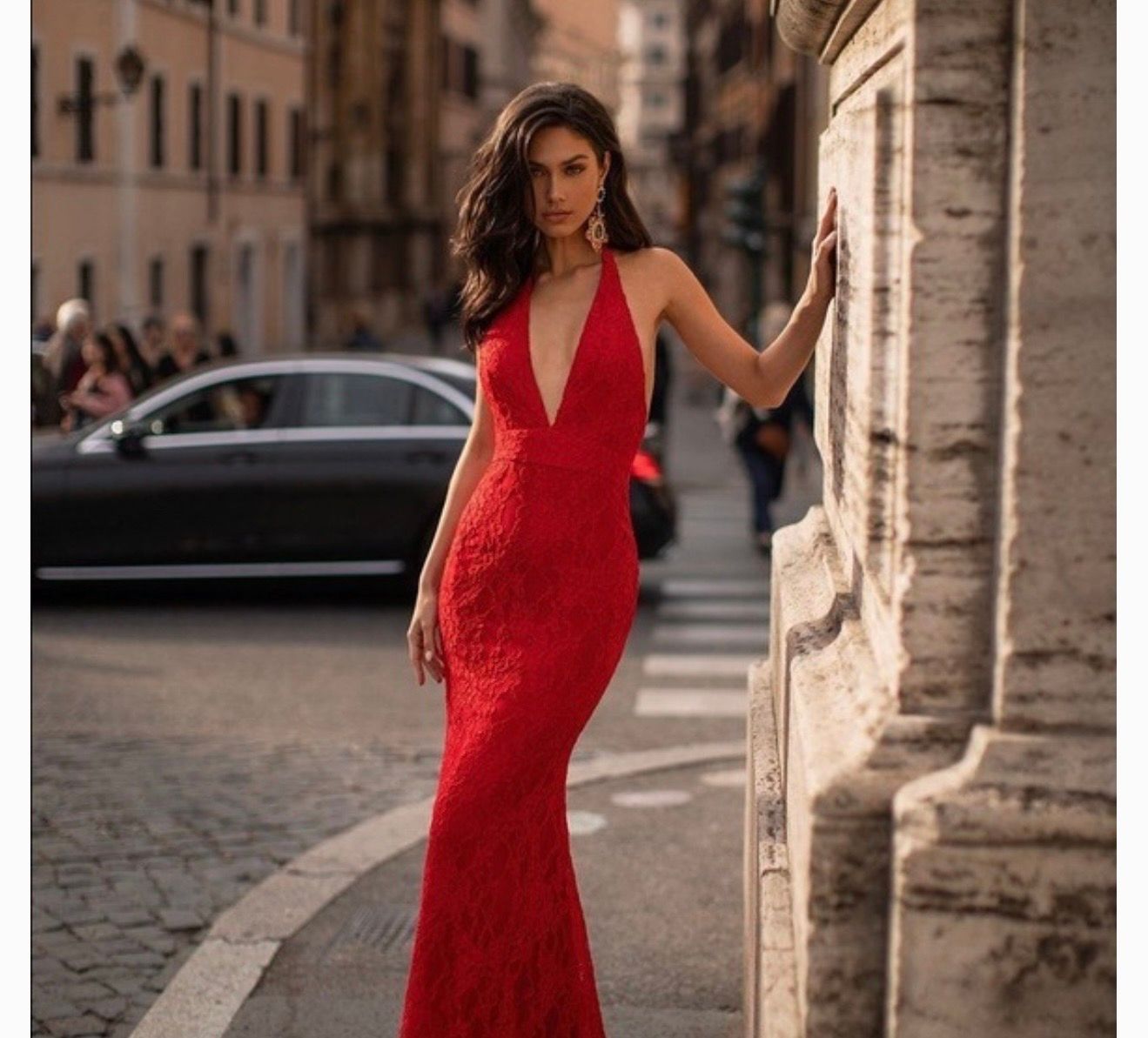 Woman in elegant red lace mermaid gown posing on a European city street.
