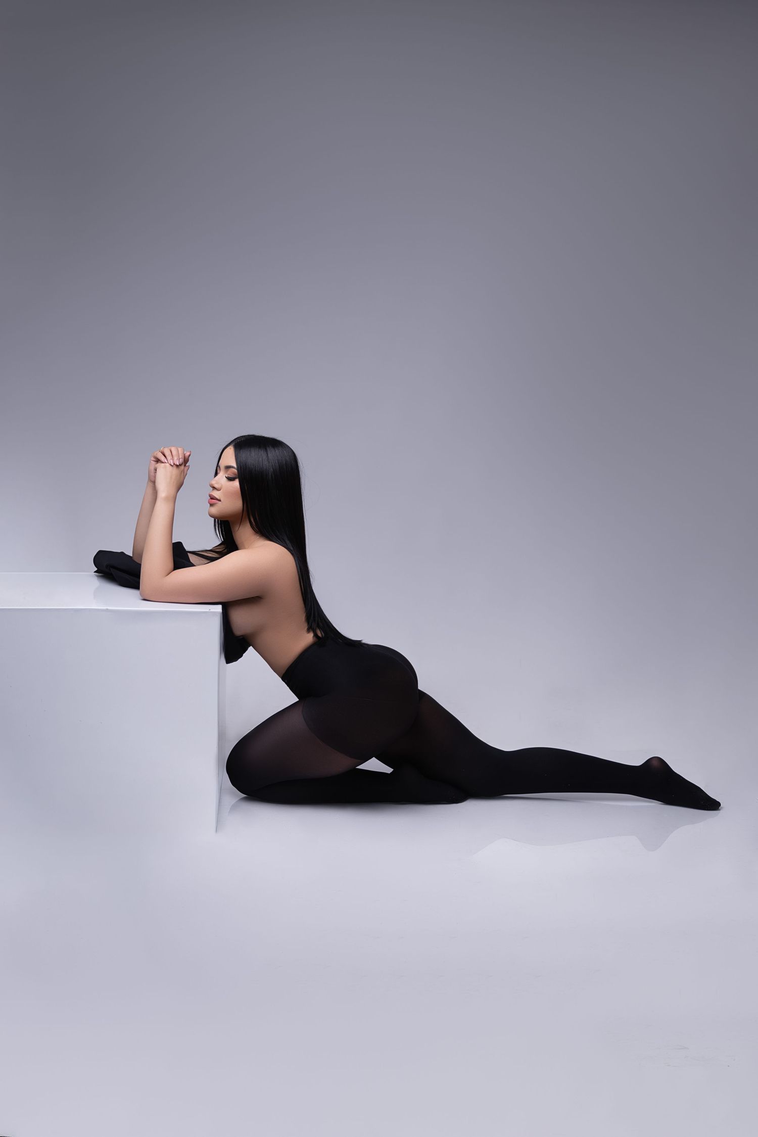 A person in black clothing lies elegantly posed on a gray seamless backdrop in a sequence of artistic shots.