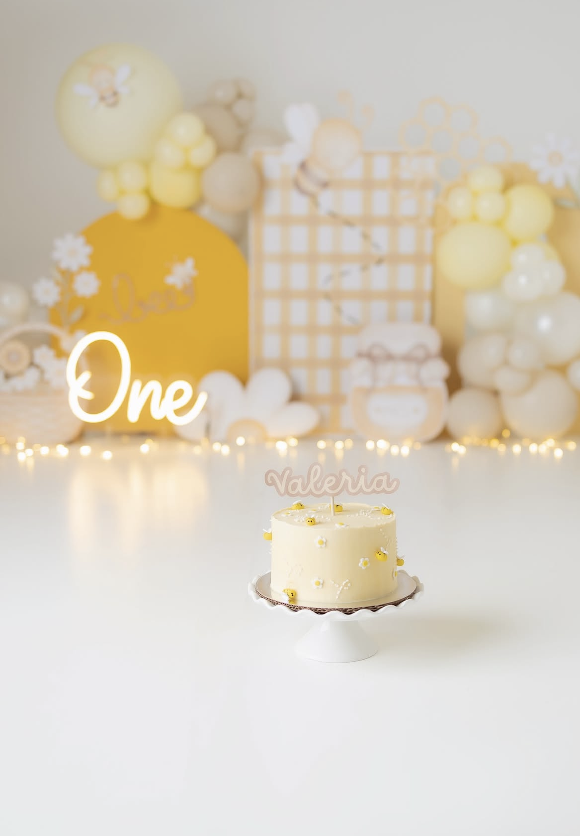 Yellow first birthday smash cake with name topper Valeria, balloon backdrop and daisy decorations.