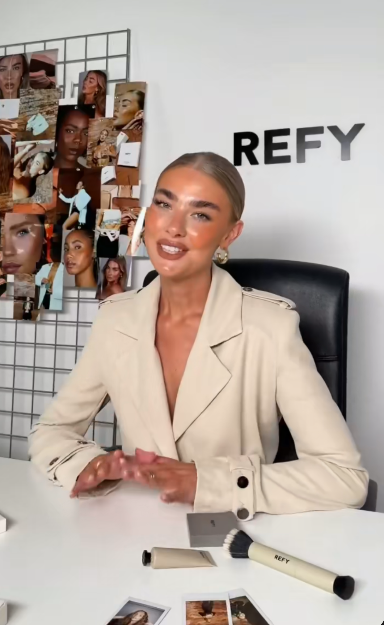 Woman in beige blazer sits at desk with REFY beauty products, mood board, and brand logo in background.