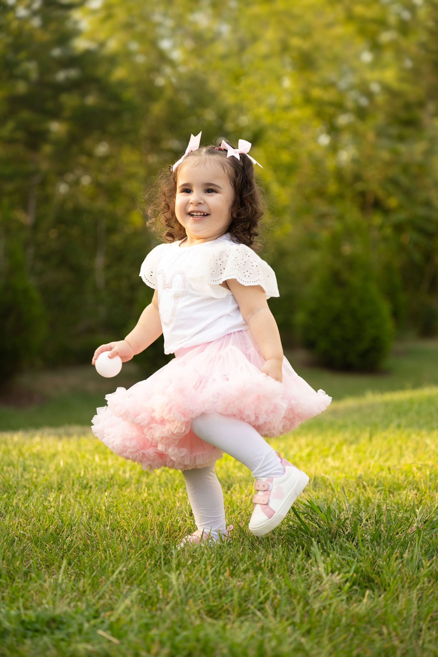 Joyful child in tutu skirt dancing outdoors in sunny garden setting.