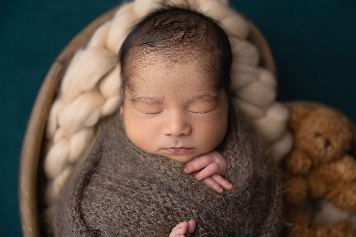 Peaceful newborn wrapped in grey knit blanket sleeping in woven basket.