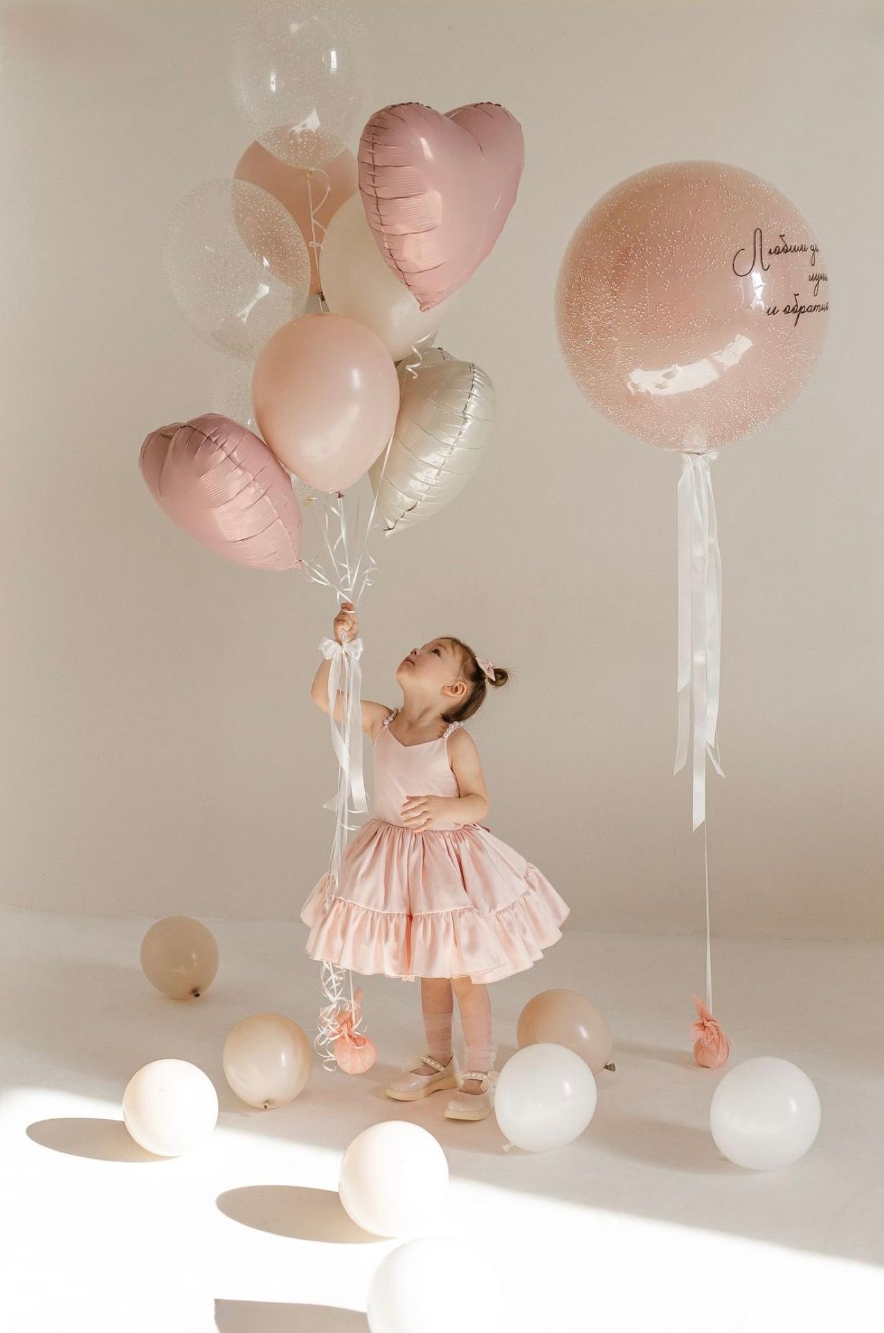 Young girl in pink dress holding heart-shaped and round balloons at a birthday party celebration.