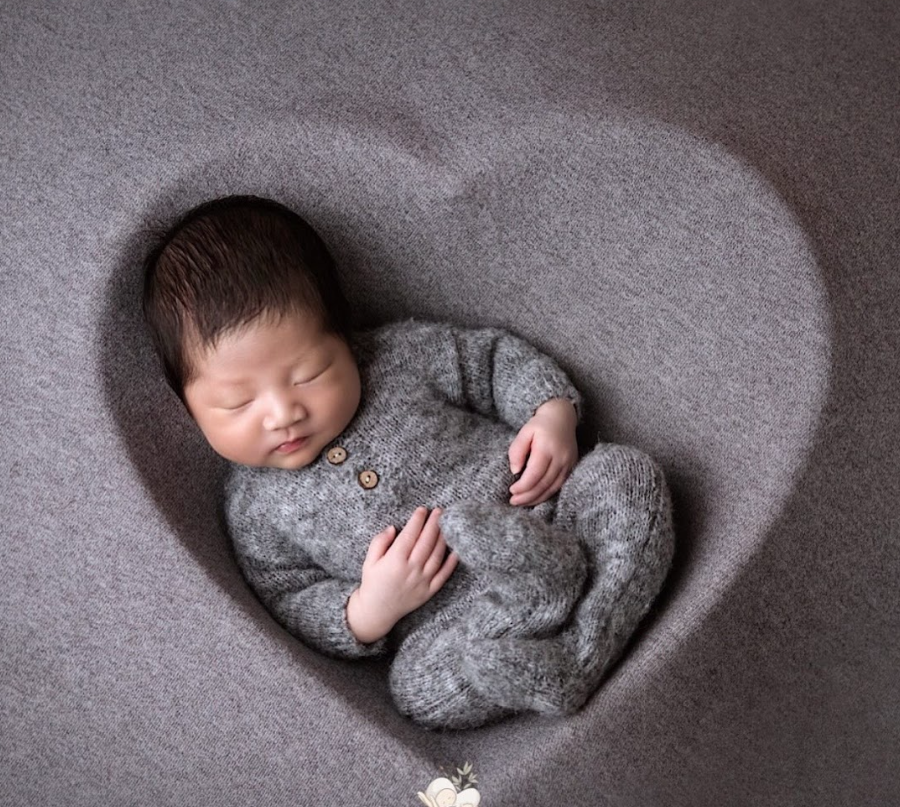 Sleeping newborn baby wearing gray outfit curled up on soft gray blanket in artistic black and white portrait.
