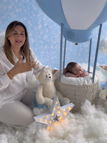 A cozy nursery scene with a white teddy bear, illuminated star light, and fluffy cloud decorations in blue tones.