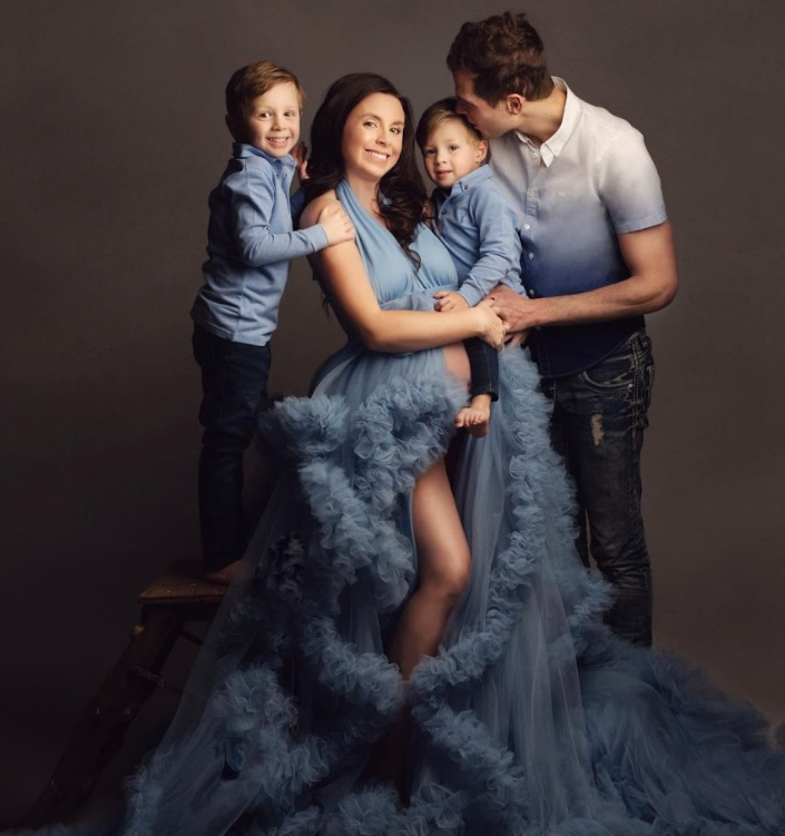 Family portrait session featuring coordinated dusty blue outfits against dark backdrop in studio setting.