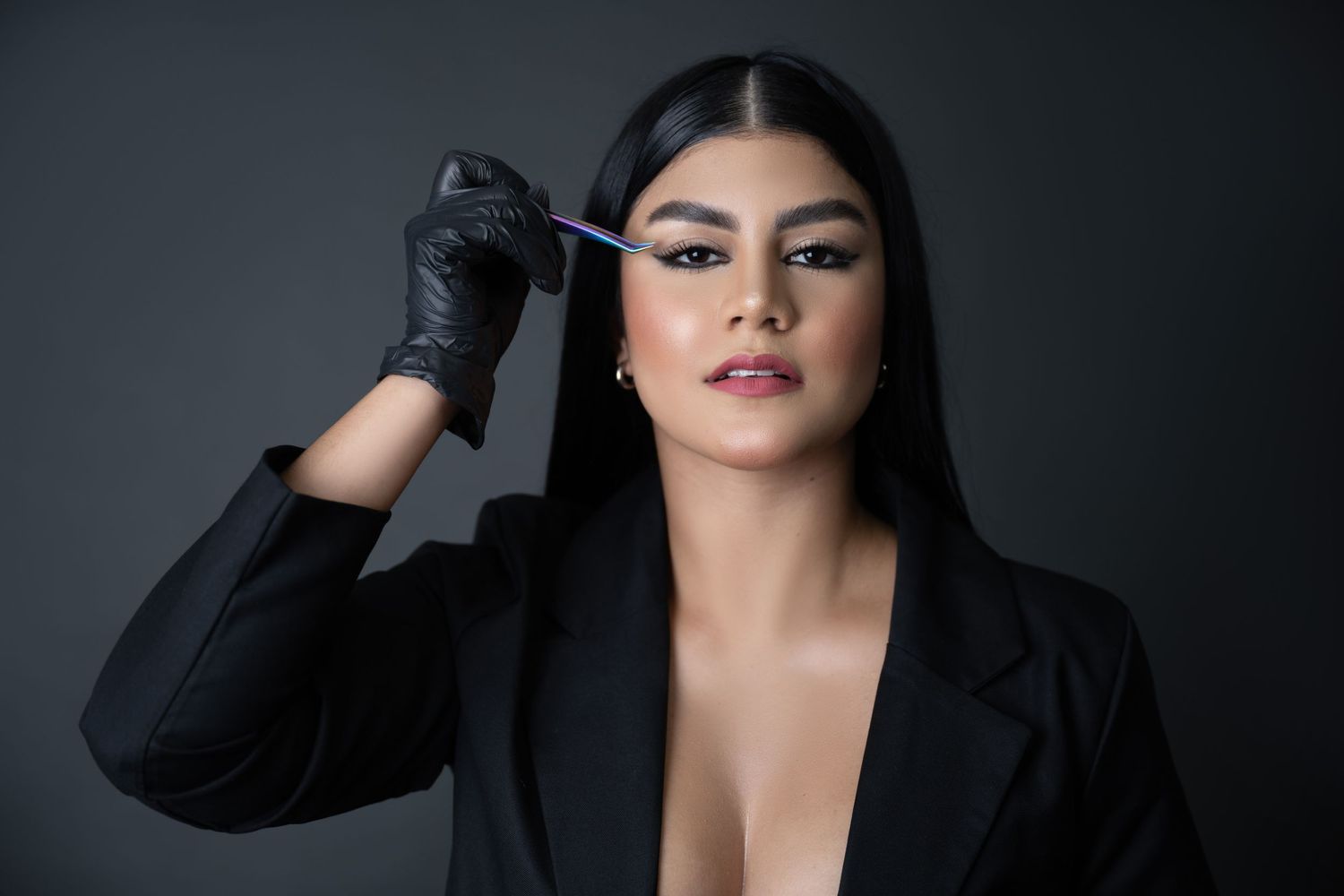 Glamorous beauty professional wearing black blazer and gloves in dramatic studio lighting.