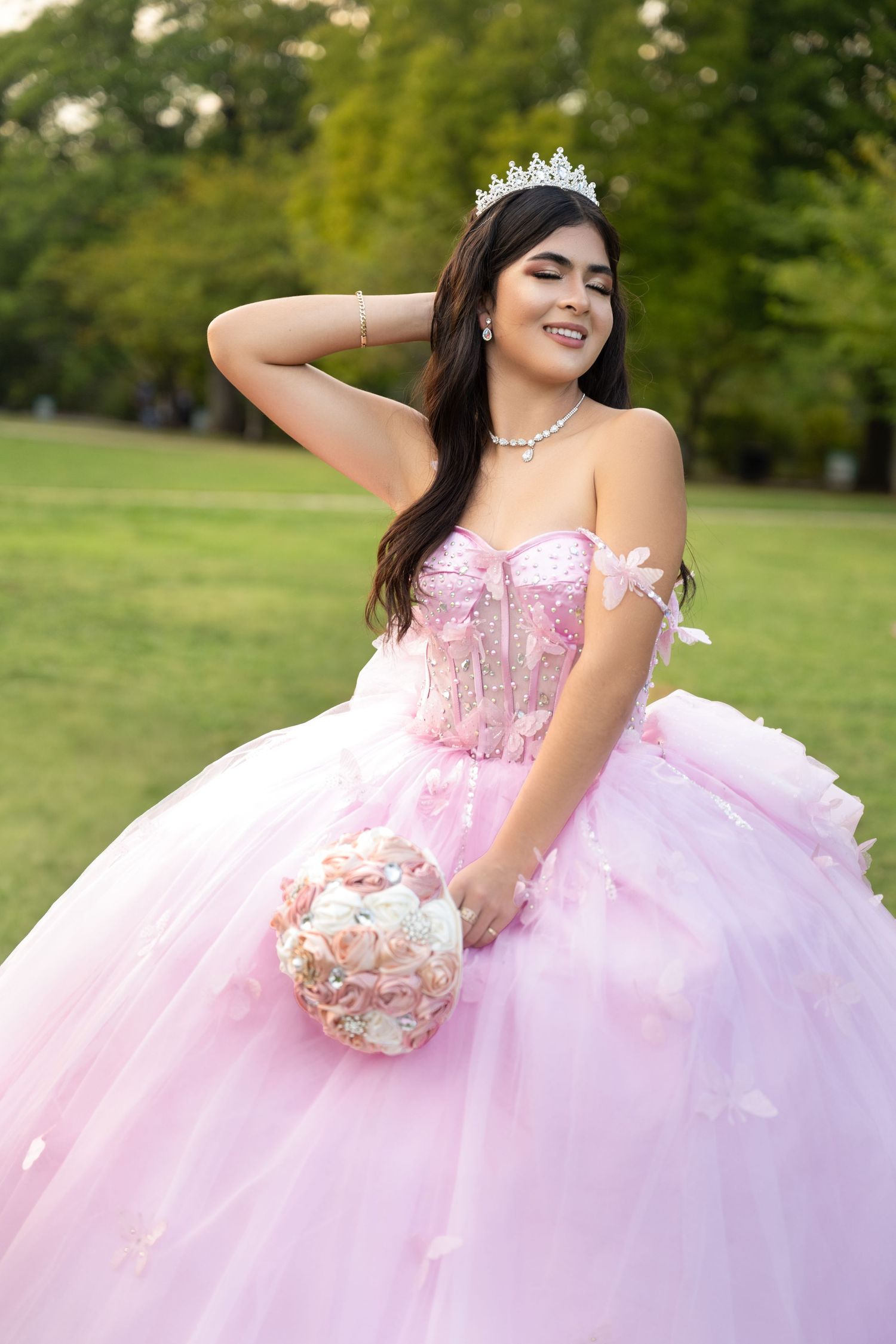 Portrait in pink princess ballgown holding floral bouquet outdoors.