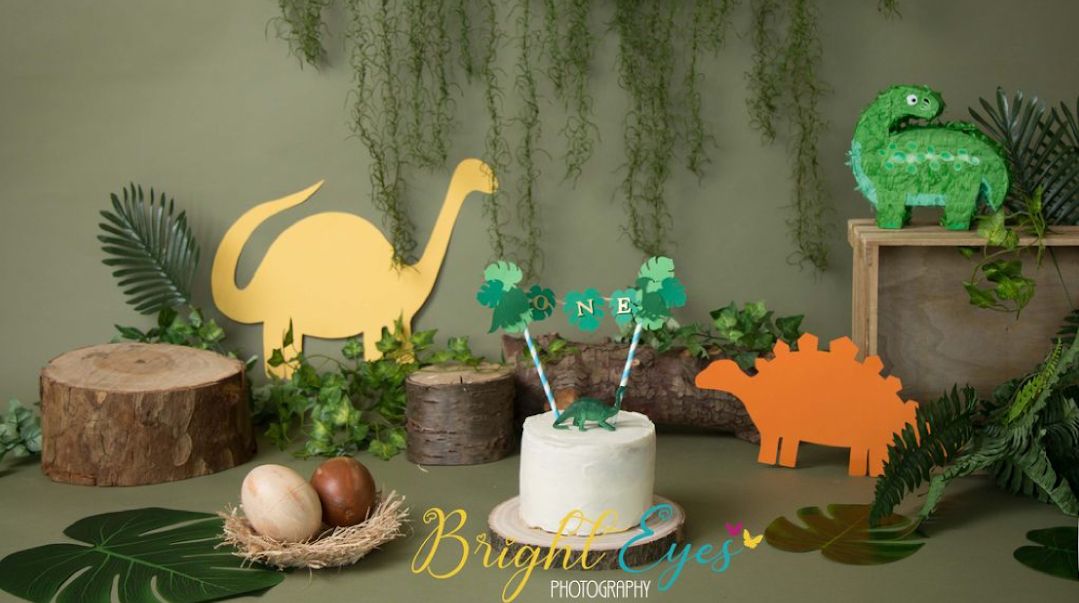Colorful wooden dinosaur decorations and plants arranged on a rustic wooden shelf with soft lighting.