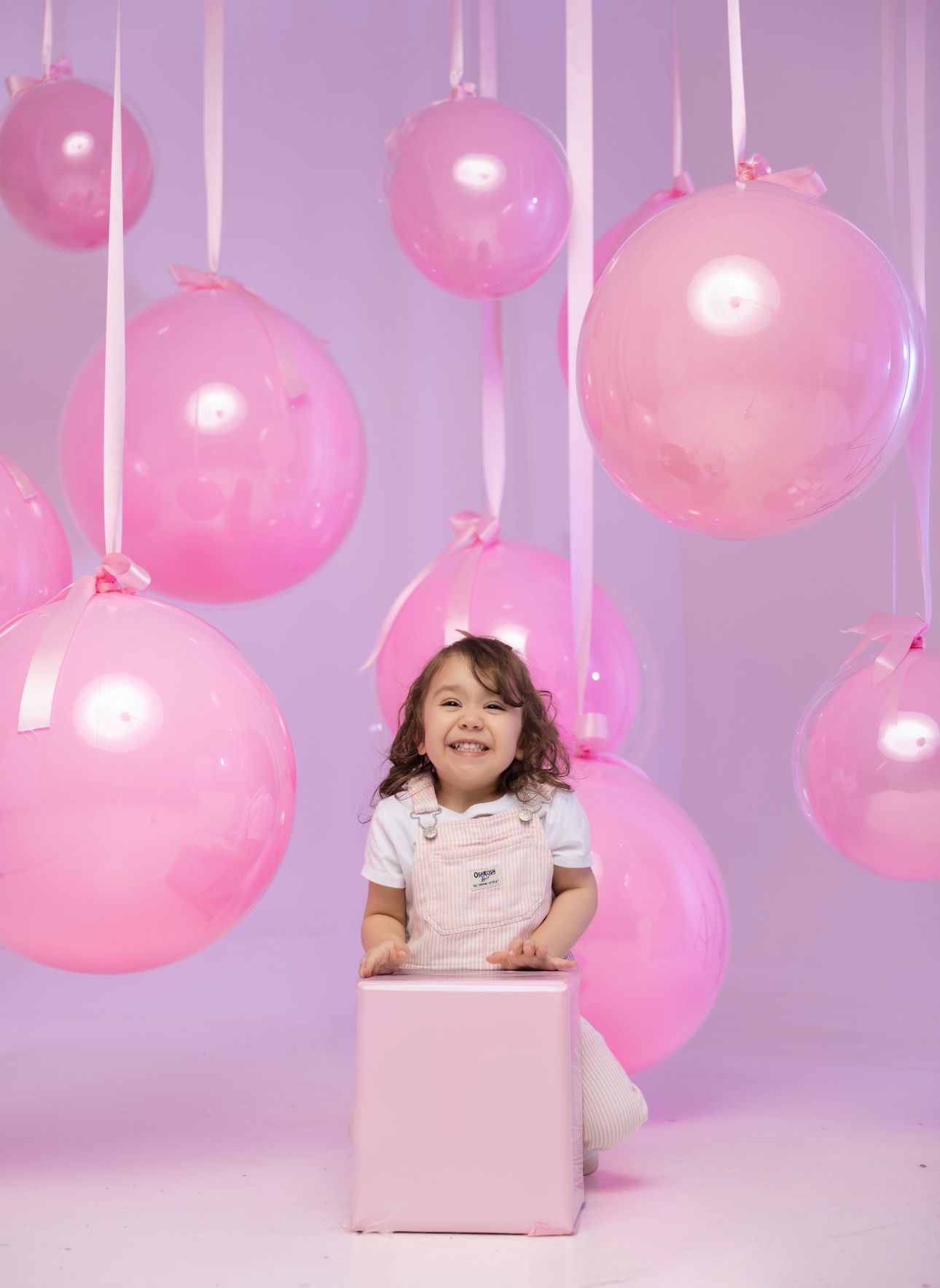 Pink balloon decorations and a box create a whimsical studio setup against a purple backdrop.