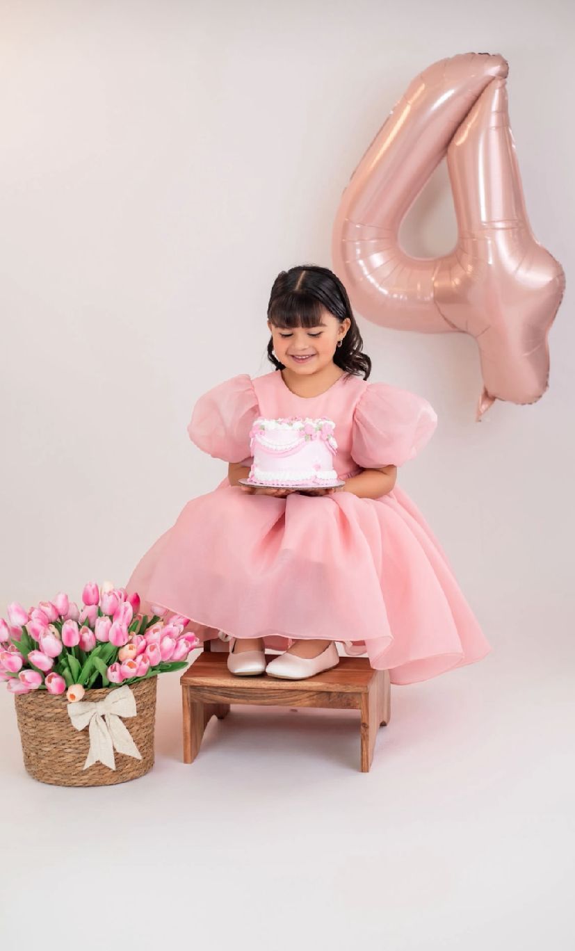 Pink birthday setup with number 4 balloon, wooden bench, and basket of pink tulips against white backdrop.