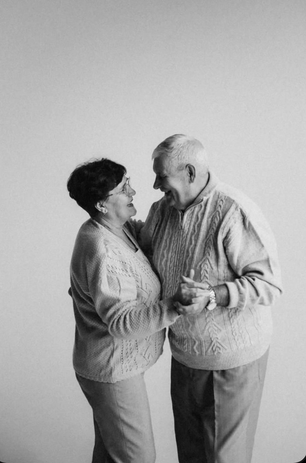 Elderly couple dancing together and holding hands in a black and white portrait photo.