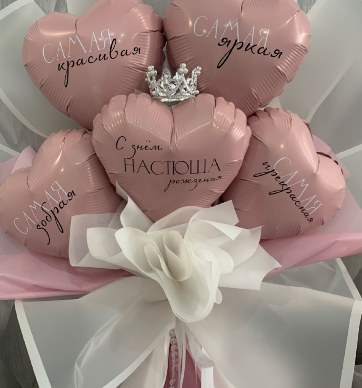 Pink heart-shaped balloons with Russian text and a crown charm arranged in a gift bouquet with white ribbon bow.