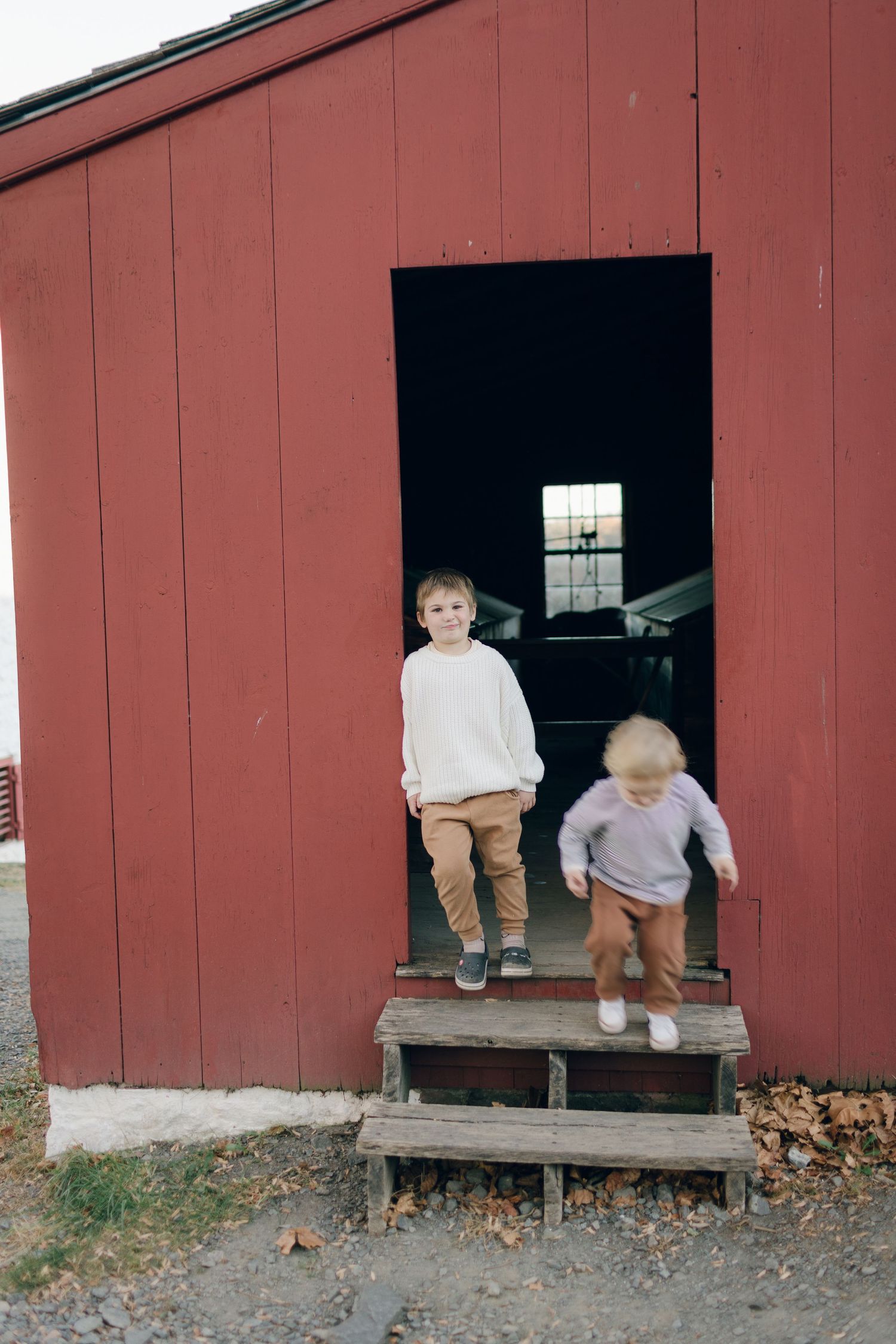 Children standing on wooden steps of red barn doorway.