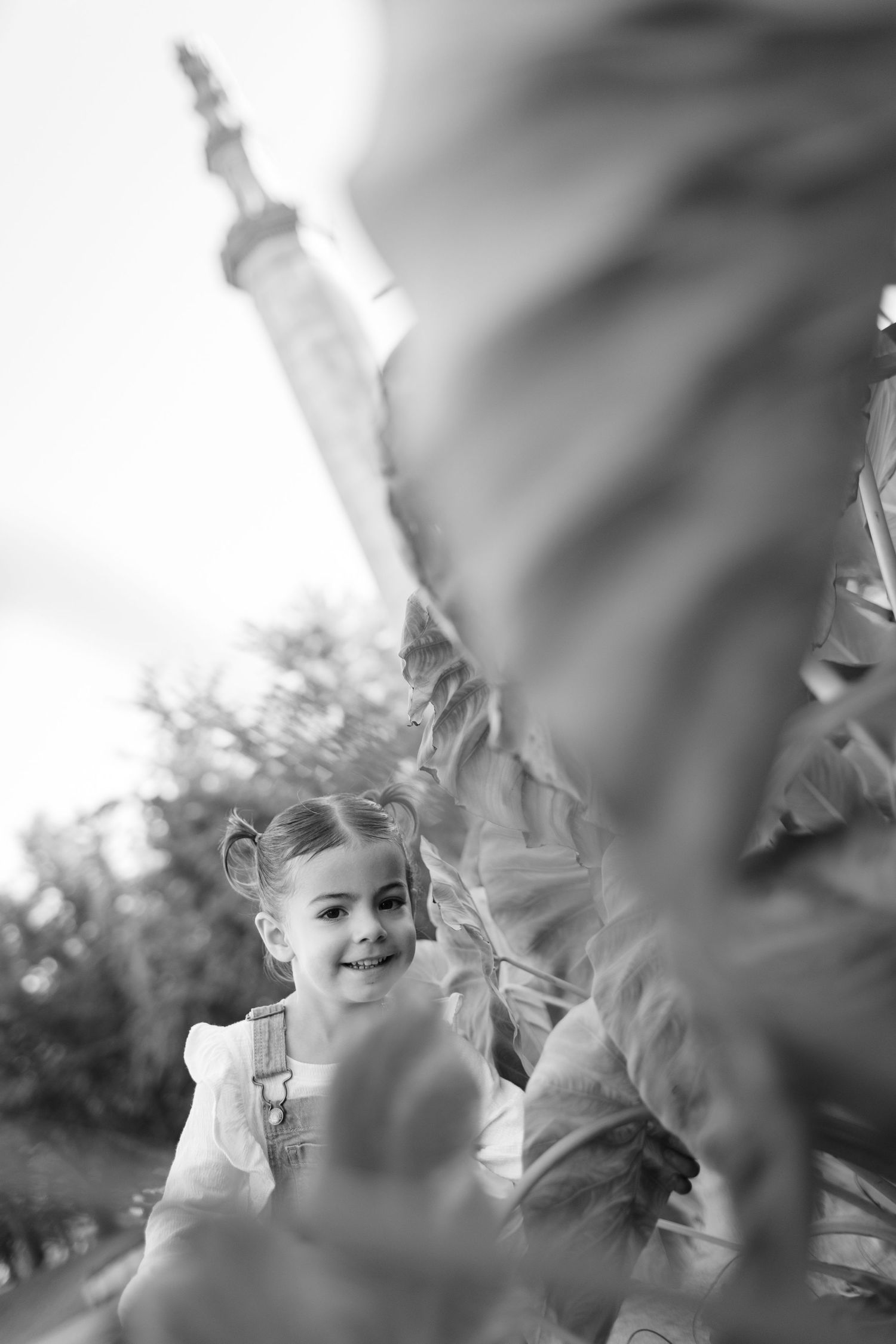 Artistic black and white close-up portrait of child smiling through leaves.