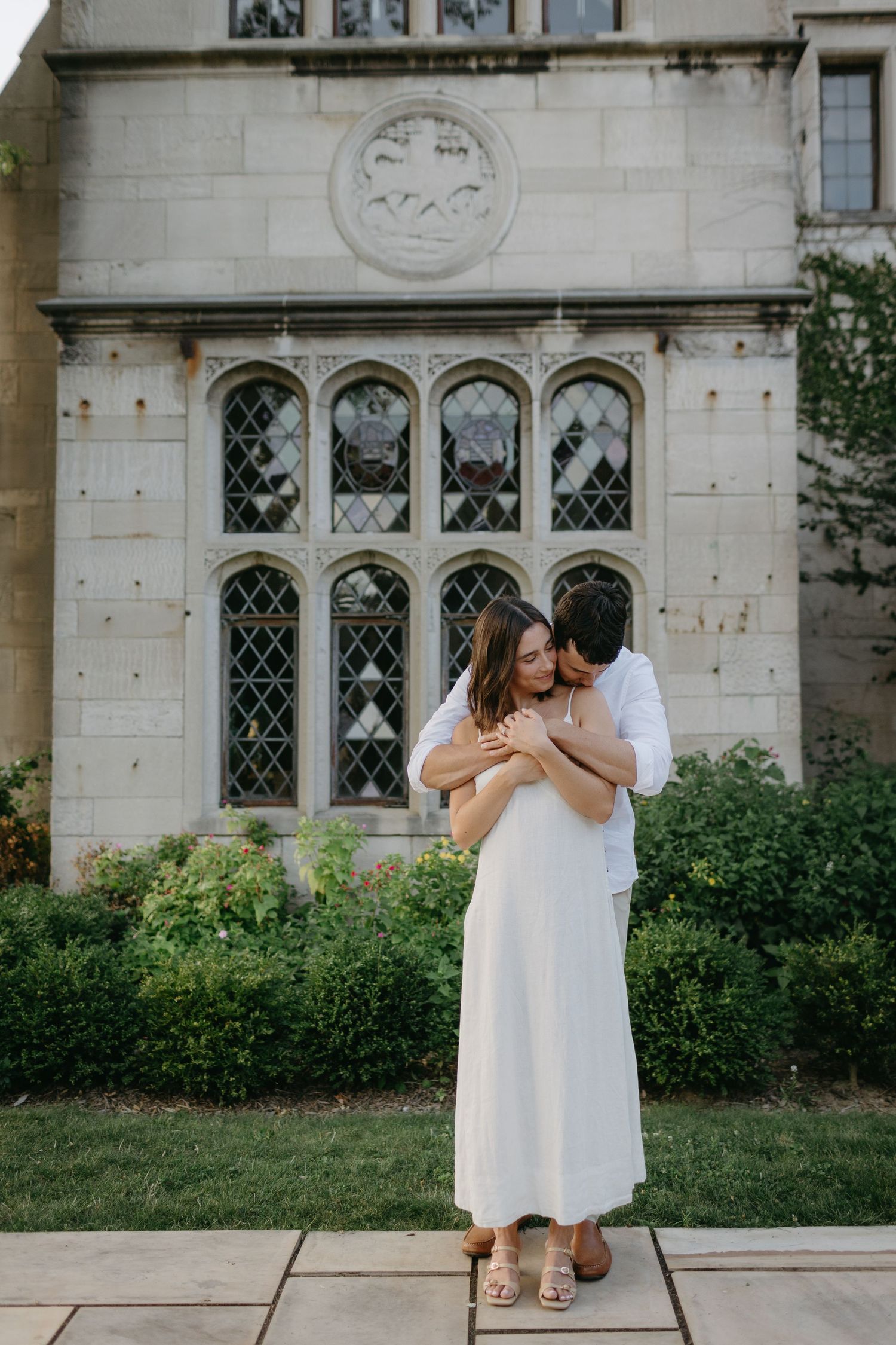 Romantic embrace in front of ornate stone church with gothic windows.