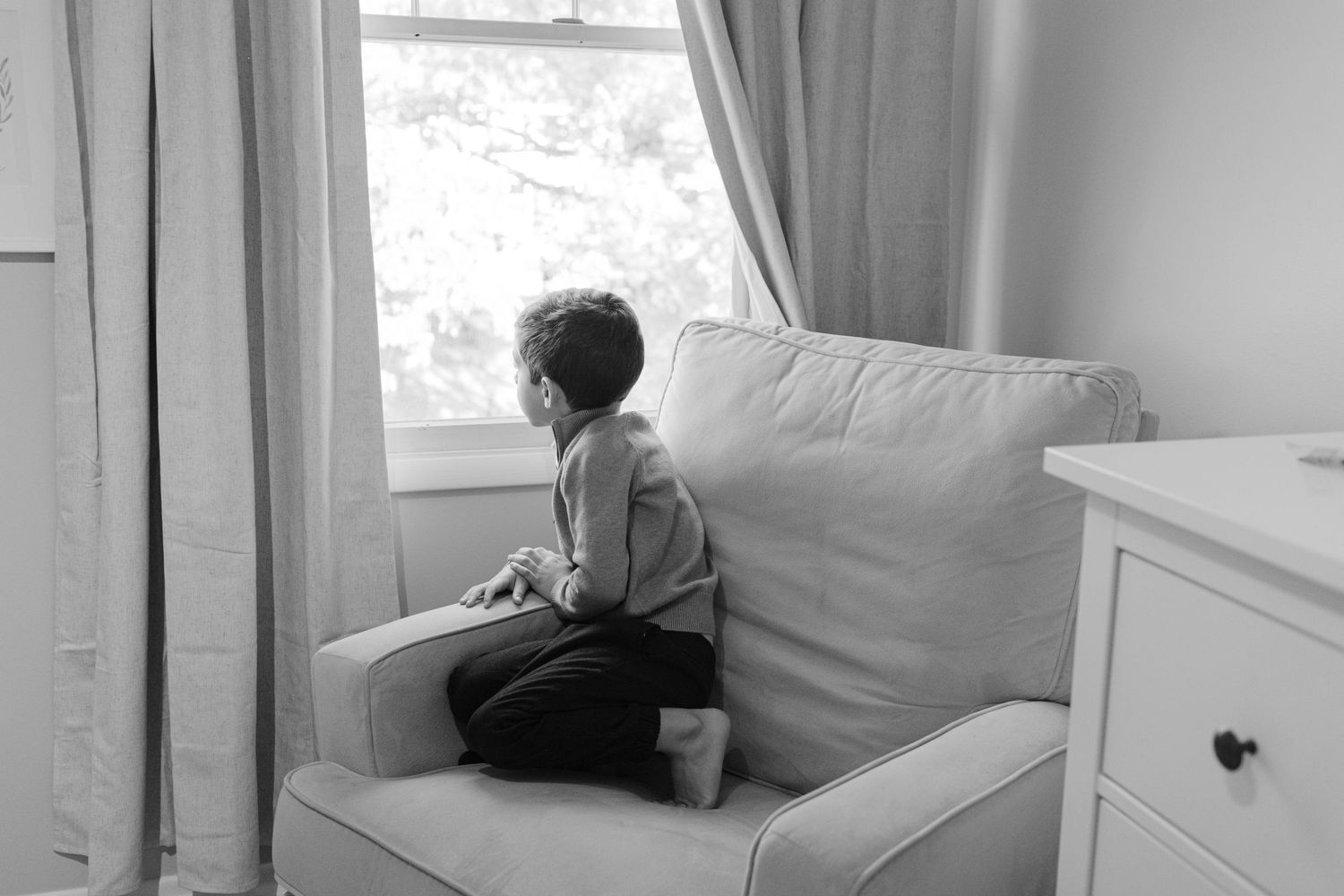 A contemplative moment looking out a bright window while seated on a white armchair.