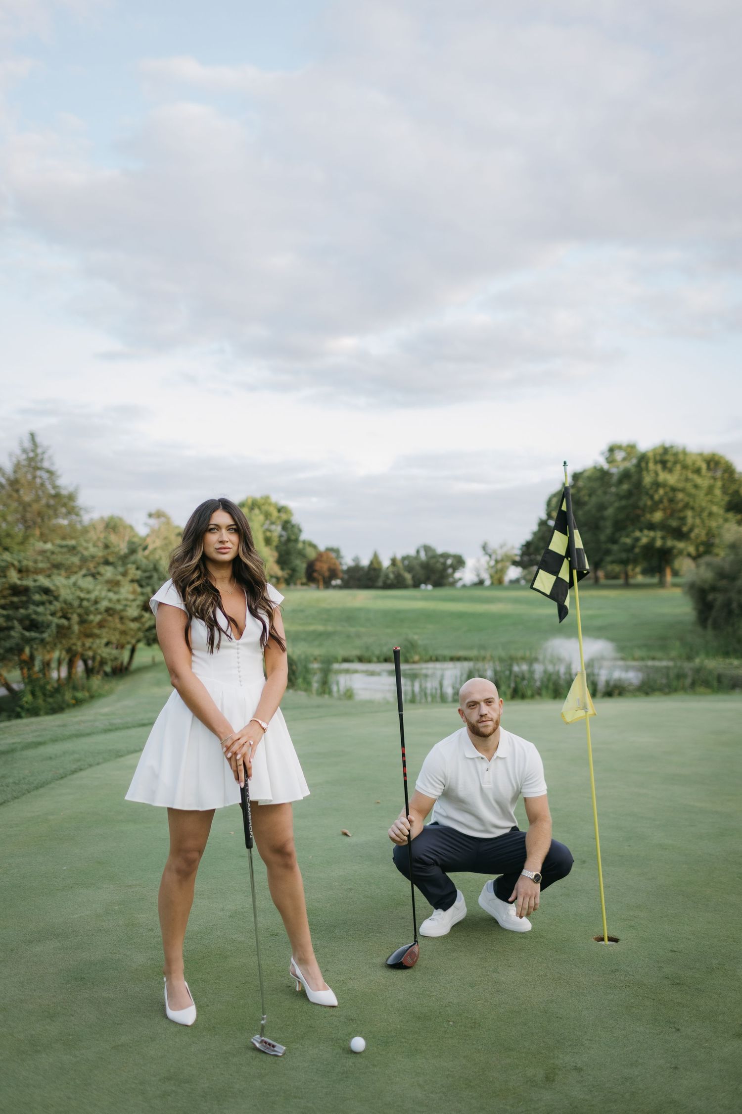 Golf course engagement photo with couple on putting green at sunset.