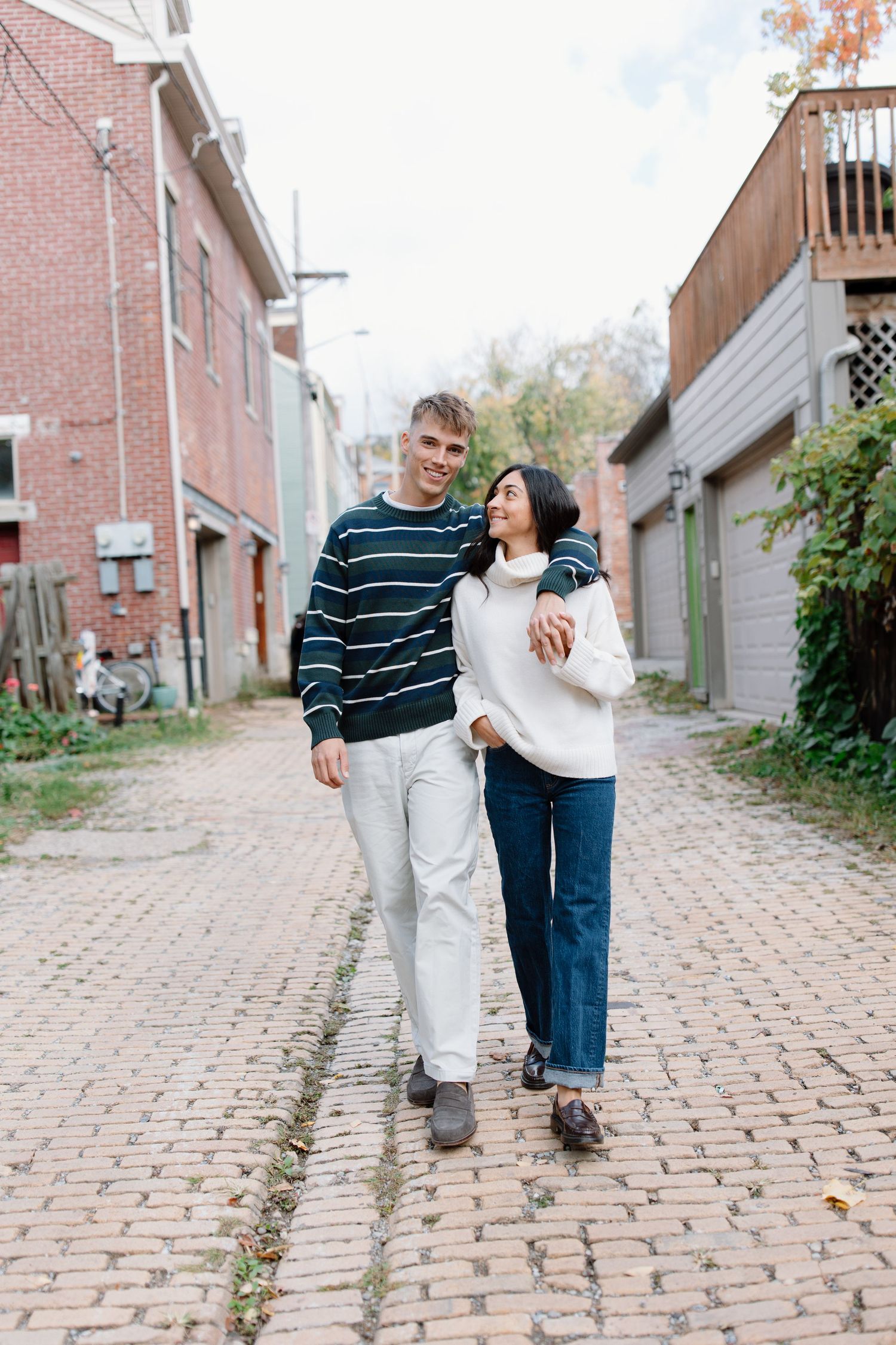 A couple walks together on a brick paved alley between buildings on an autumn day.
