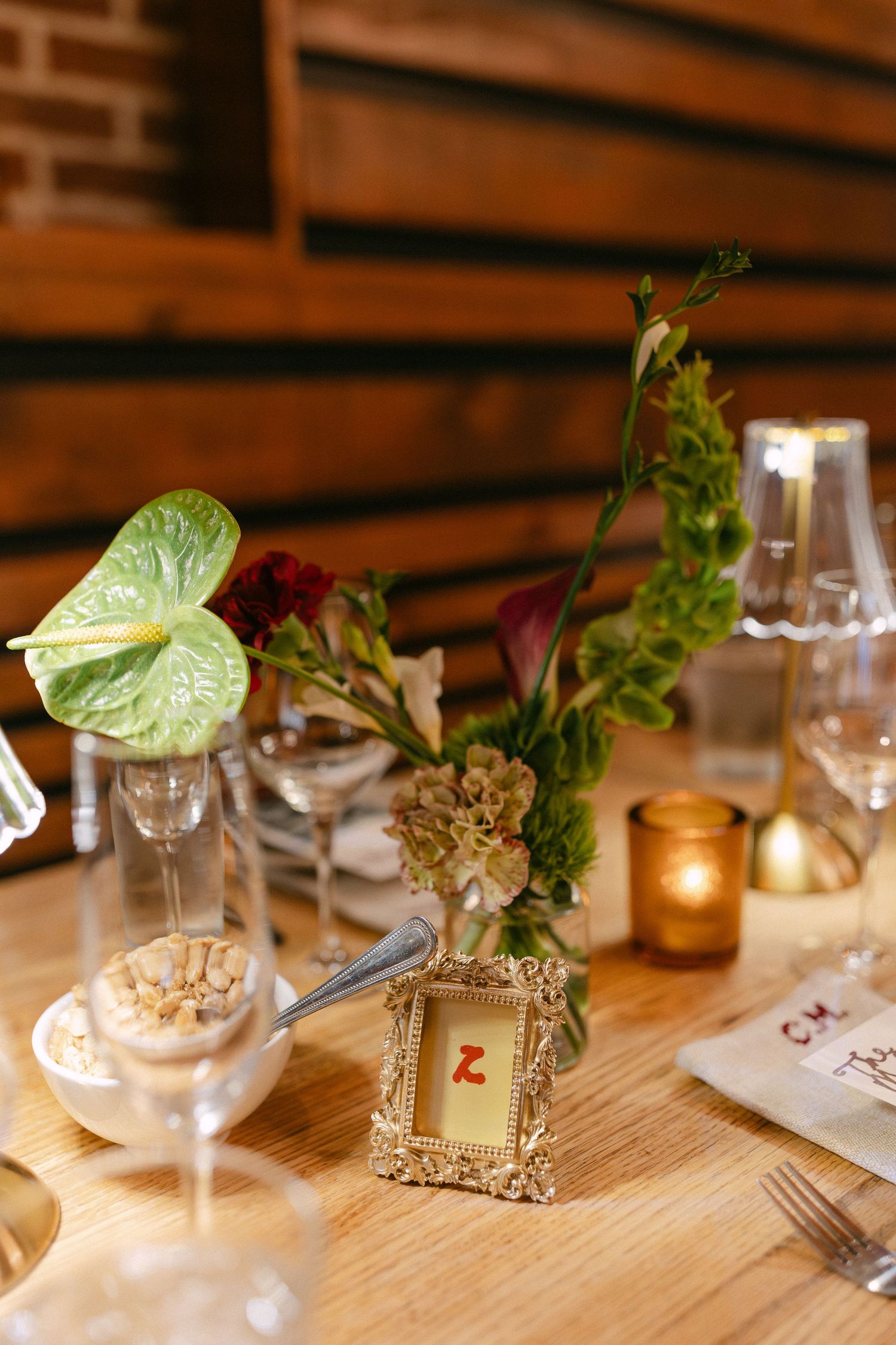 Elegant table setting with small floral arrangements in vintage frames and wine glasses on a wooden surface.