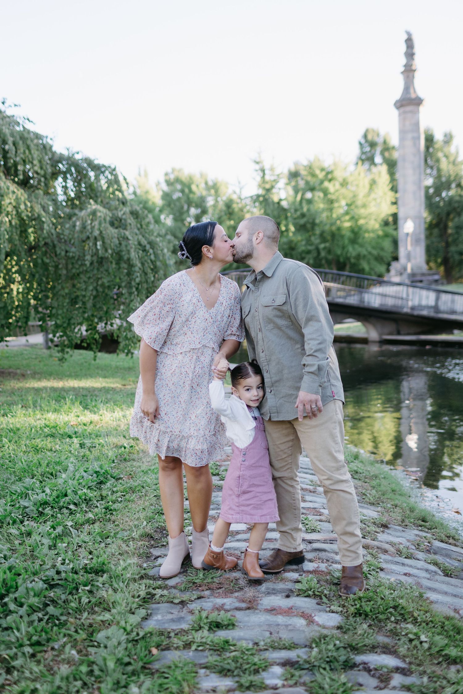 Family standing together by historic bridge and monument in park setting.