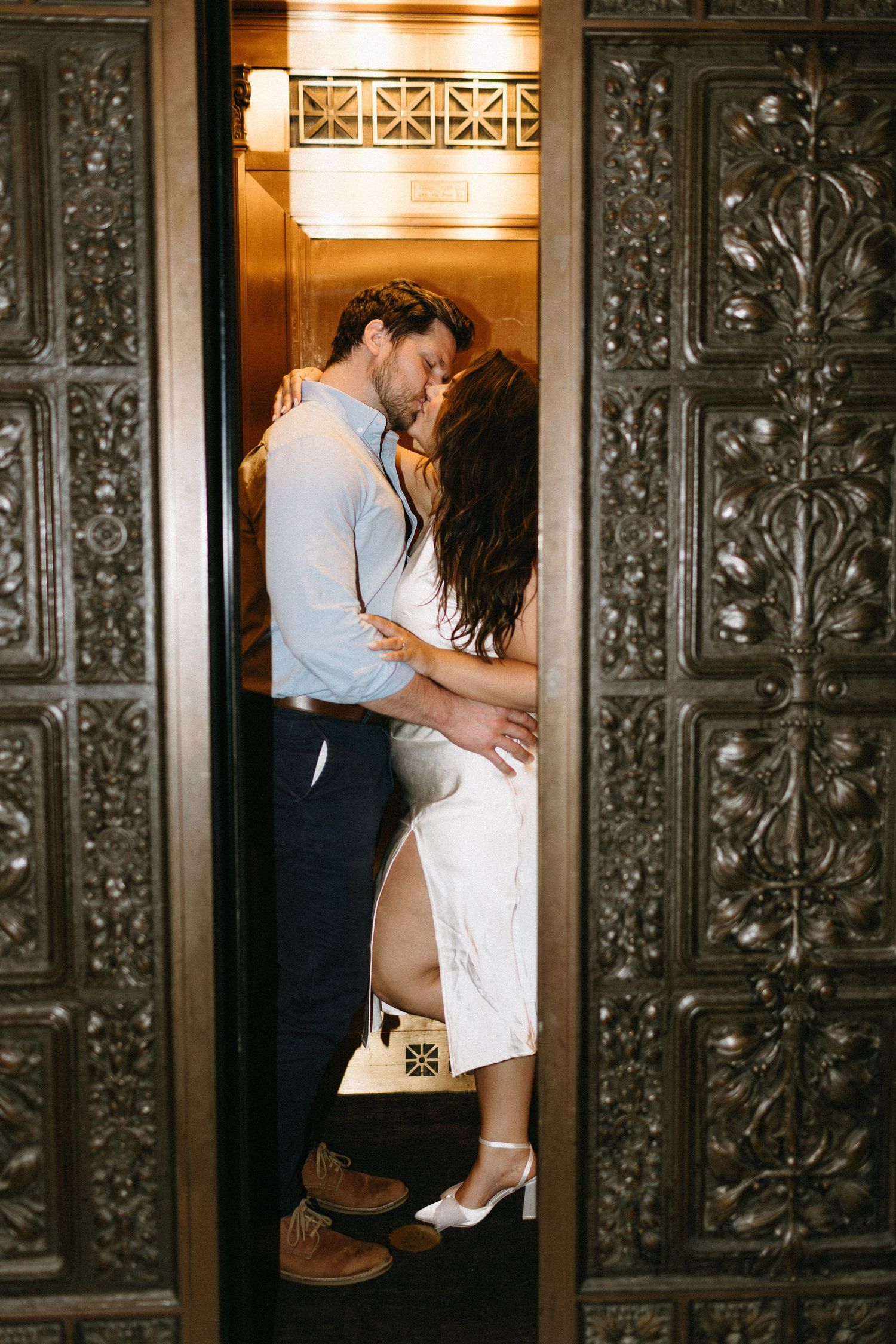 Romantic moment captured in vintage elevator with ornate metalwork details.