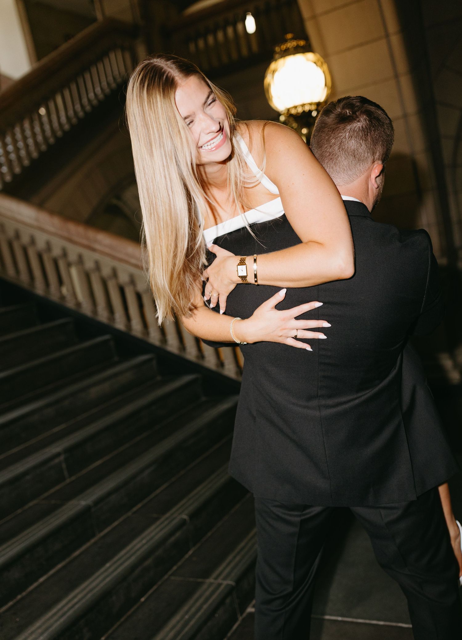 A joyful couple sharing a romantic moment with an embrace on an elegant staircase with pendant lighting.