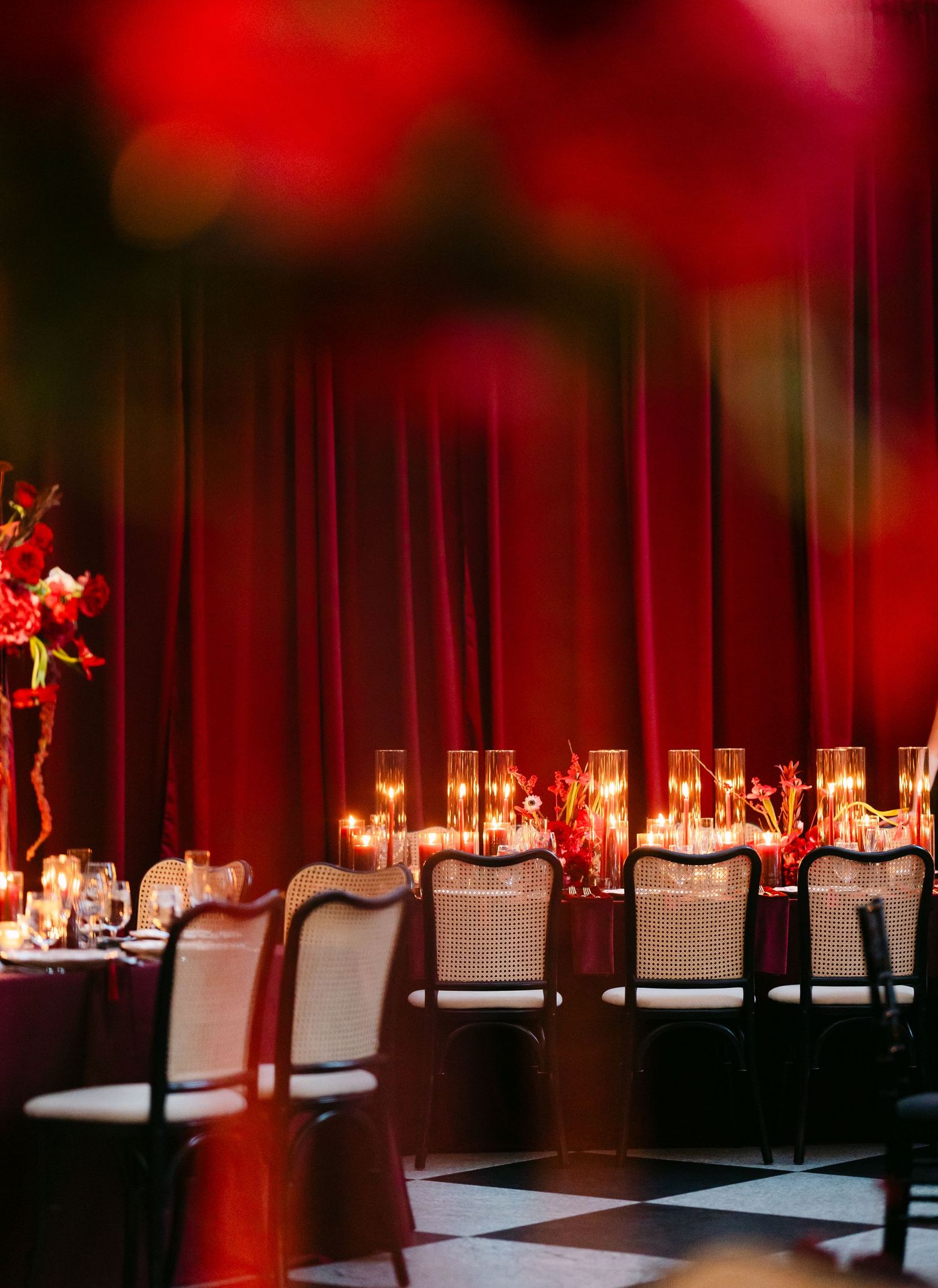 Long banquet tables with white tablecloths and elegant place settings are illuminated by dramatic red lighting in an event space.