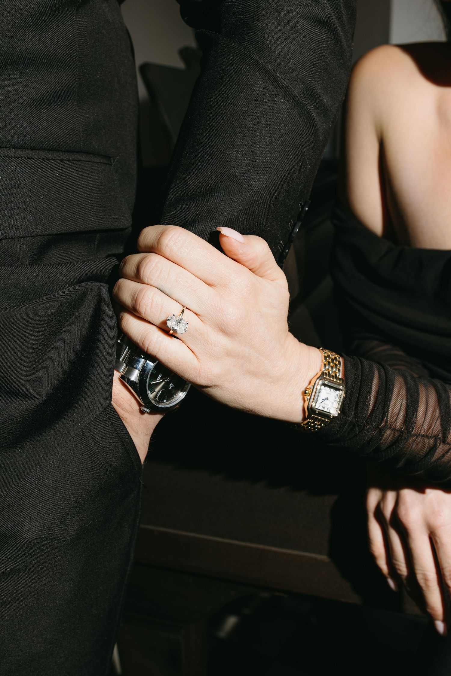 Close-up shot of hands with engagement ring and watch against formal attire.