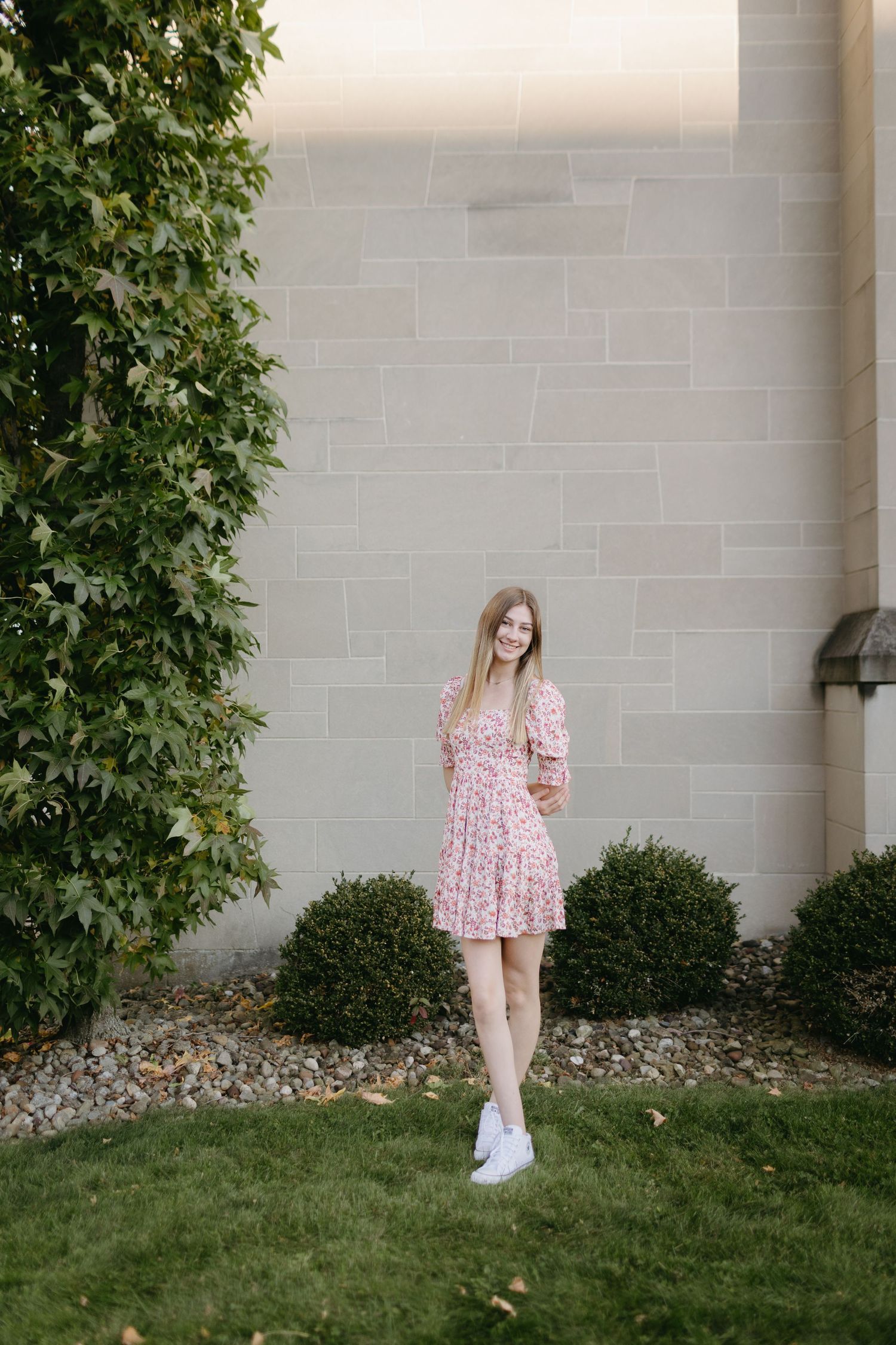 A pink floral dress ensemble paired with white sneakers against a stone wall backdrop.