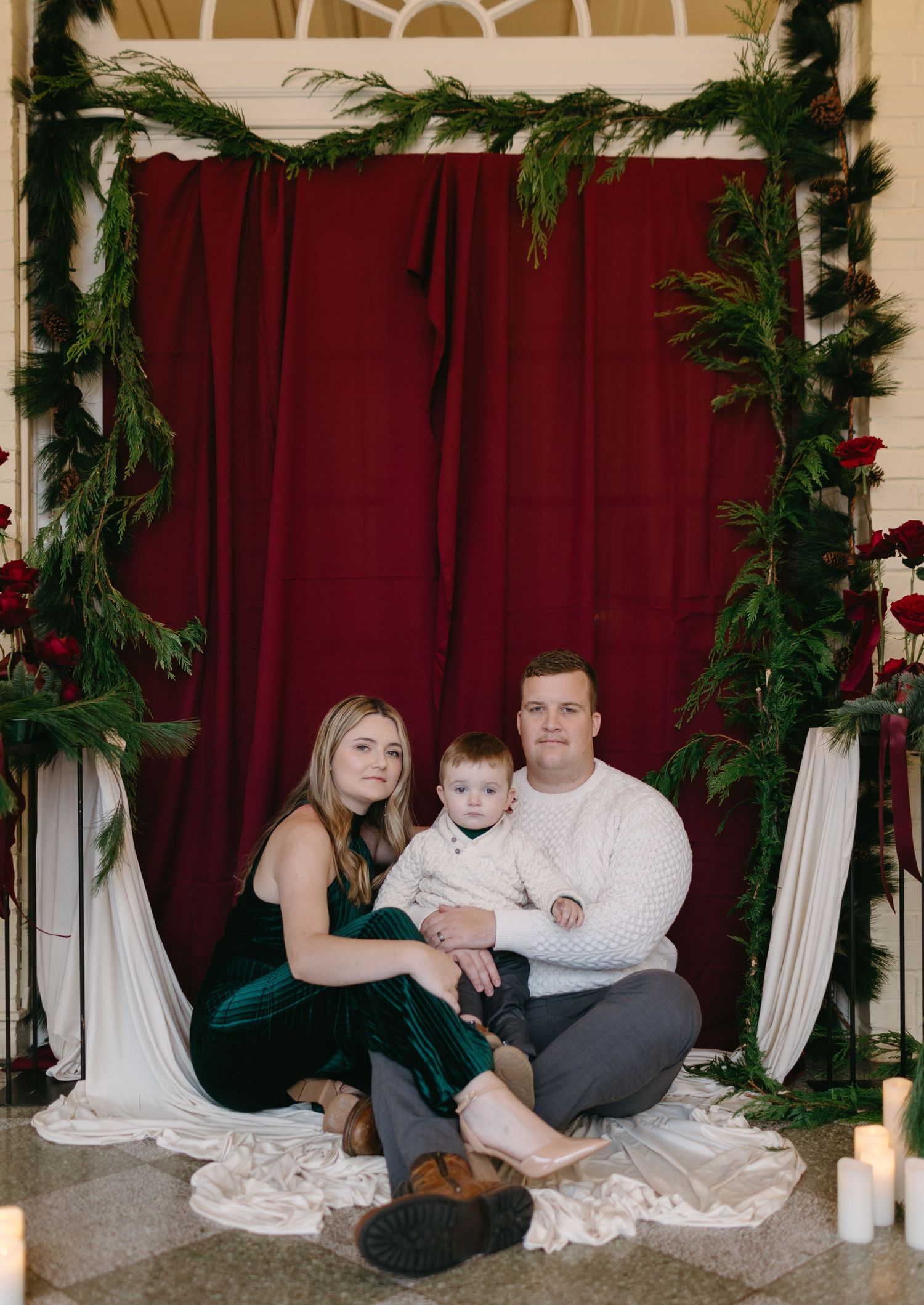 Holiday family portrait with red curtain backdrop and evergreen garland decorations.