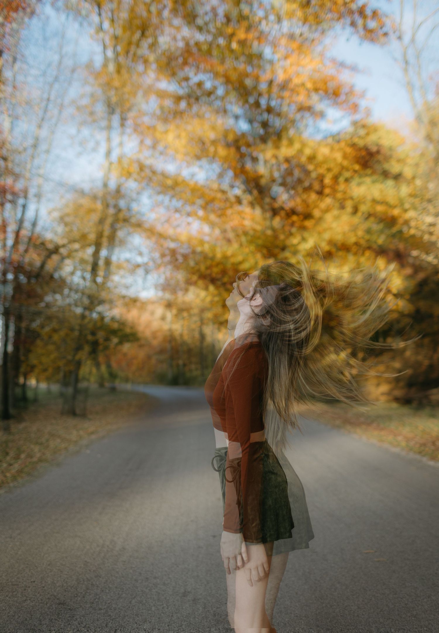 Motion blur portrait on autumn road with golden trees and soft bokeh effect.