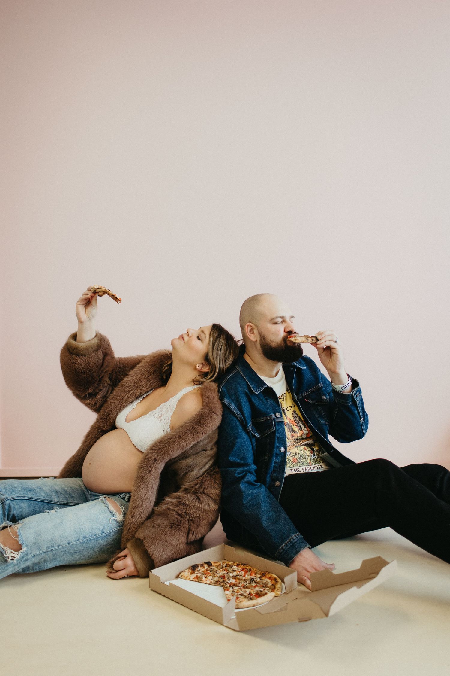 A casual maternity photo showing a couple sharing pizza while sitting on the floor.